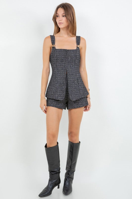 Woman wearing a tweed corset top and matching mini shorts with metal trim, styled for a modern elegant look.