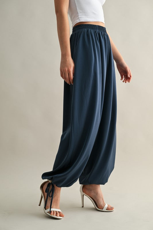 Woman wearing satin balloon harem pants with an adjustable hem, styled for an elegant and modern day-to-night look.