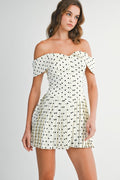 Woman wearing an off-shoulder polka dot pleated mini dress styled for a playful and elegant day-to-night look.