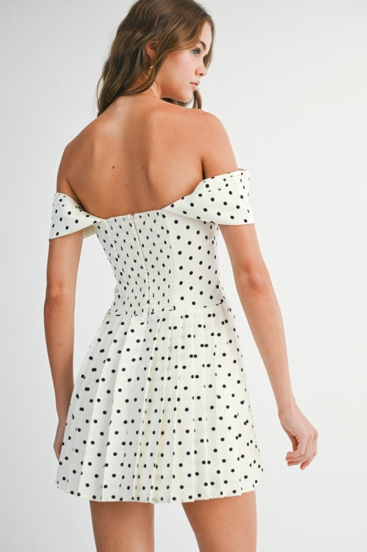 Woman wearing an off-shoulder polka dot pleated mini dress styled for a playful and elegant day-to-night look.