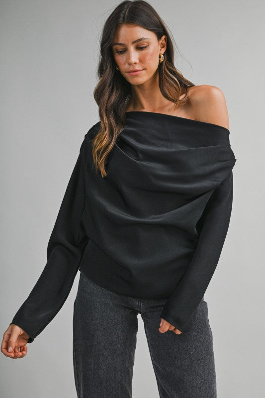 Woman wearing a one-shoulder draped top with an elegant asymmetrical neckline and flowing fabric, styled for a chic day-to-night look.