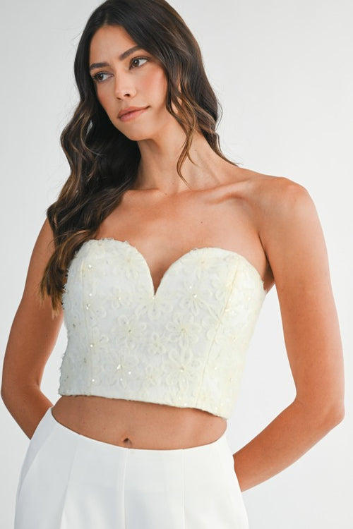 Woman wearing a strapless mesh top with 3D floral appliqués and sweetheart neckline, styled for an elegant and statement-making look.