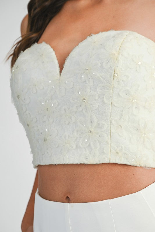 Woman wearing a strapless mesh top with 3D floral appliqués and sweetheart neckline, styled for an elegant and statement-making look.