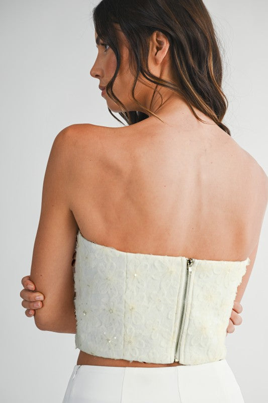 Woman wearing a strapless mesh top with 3D floral appliqués and sweetheart neckline, styled for an elegant and statement-making look.