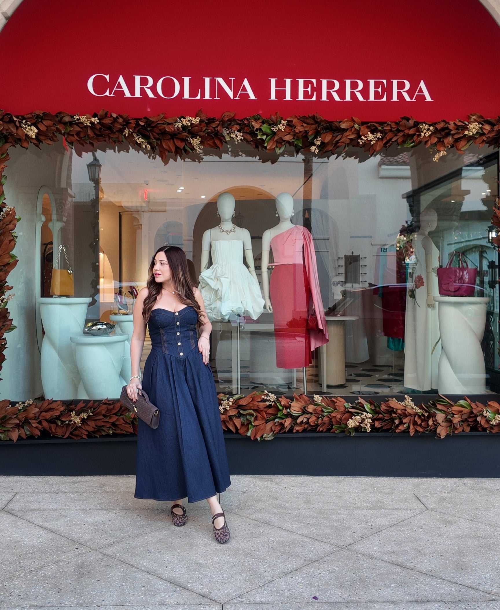 Woman in a blue dress standing in front of a Carolina Herrera store entrance.